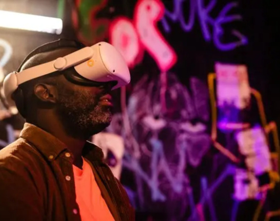 A person standing before a graffitied backdrop wears large VR goggles.