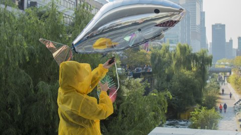 A person dressed in a yellow mac holds up a shiny silver balloon. It is a shark.