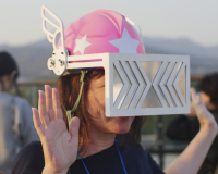 A close up of a person holding their hands up while wearing a pink helmet with silver visor. 
