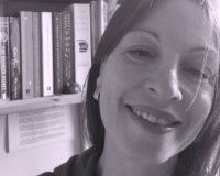 Black and white photo of dark haired white women smiling with book on shelf behind her