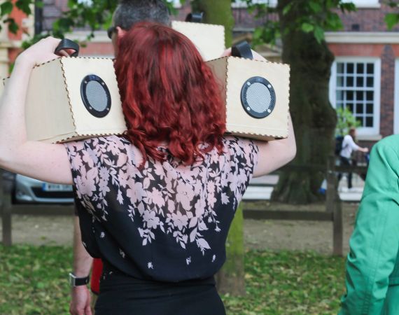 Verity holding two speaker boxes from Duncan Speakman's 'A Folded Path' up to her ears