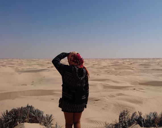 Back of a woman with a headscarf looking in the distance in a desert