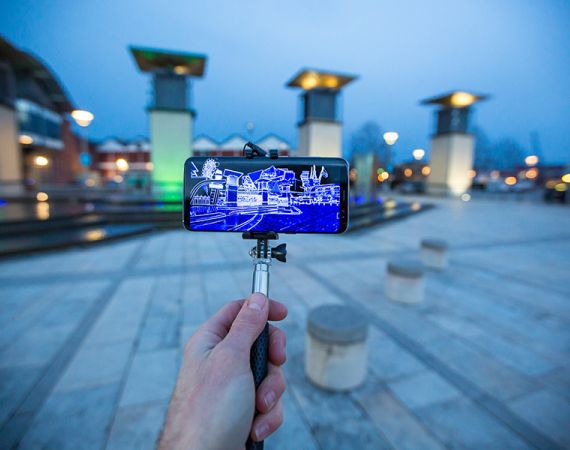 Hand holding mobile device with selfie stick in Millennium Square