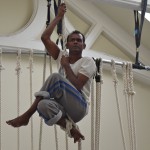 ramesh main rope small Ramesh Mayyappan up a rope - he is sitting holding the rope with his legs crossed in front of him.
