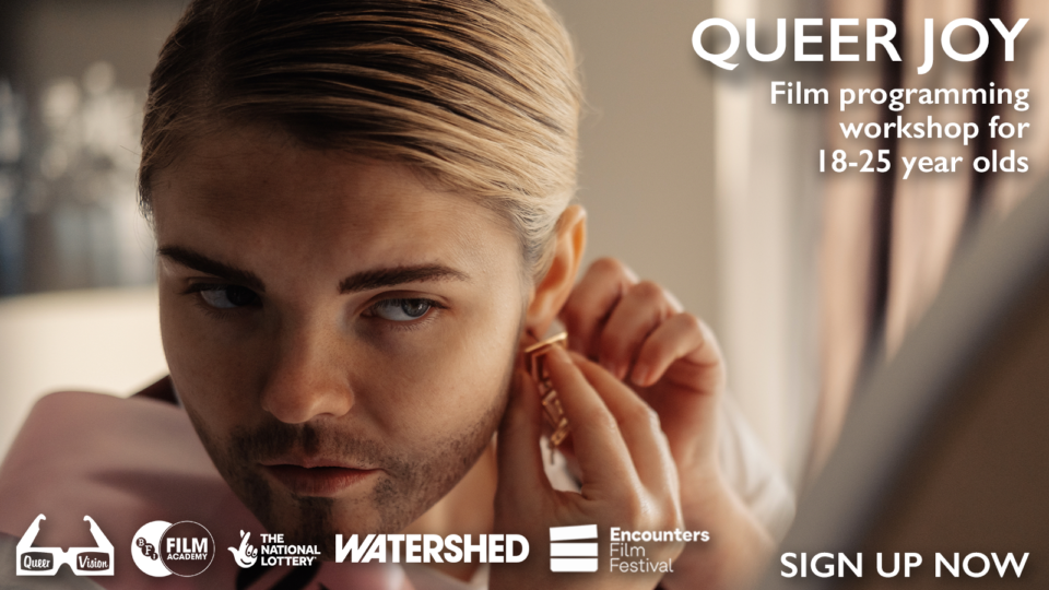 A drag artist putting on an earring in front of a beige background. Text reads: queer joy film programming workshops for 18-25 year olds. Sign up now