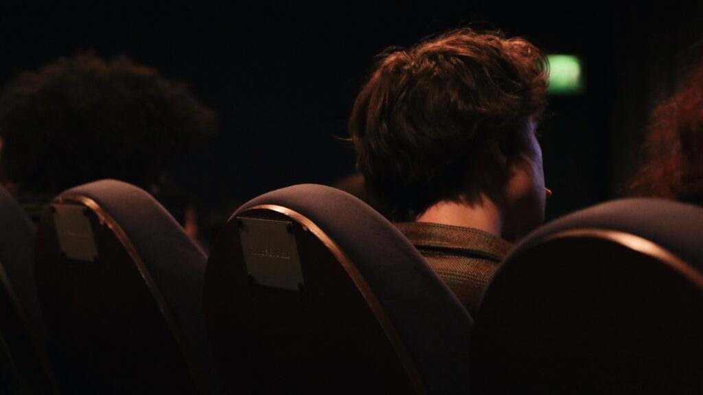 A row of cinema seats viewed from behind with a male figure sat in the middle seat