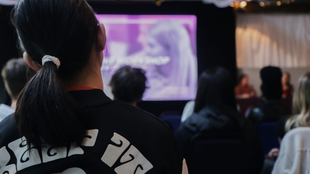 A large room of seated people, with a purple screen in the front