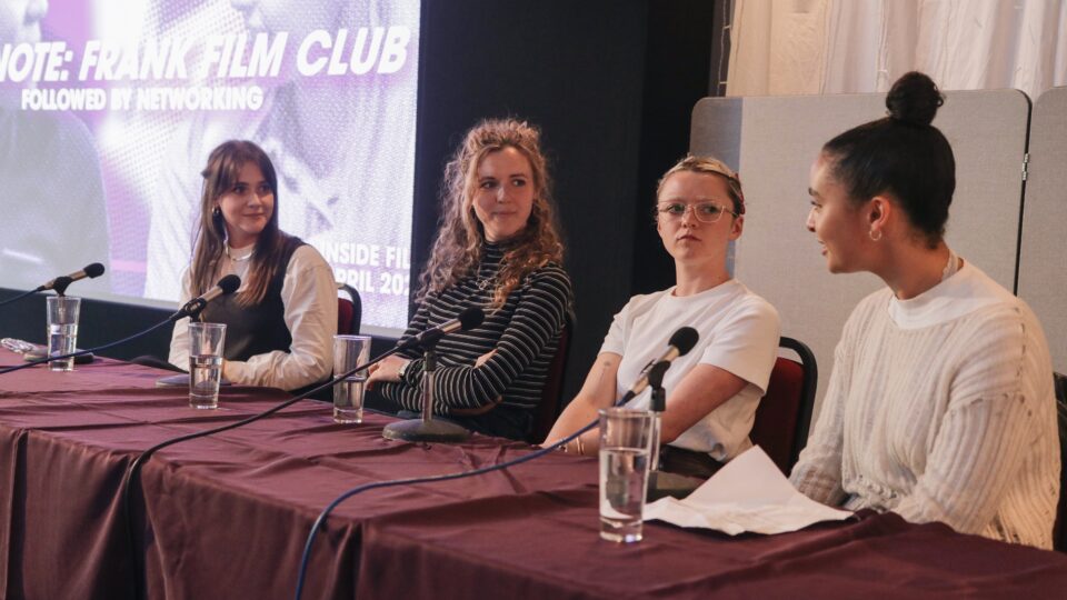 A panel of four people sat at a table with a purple slide projected behind them