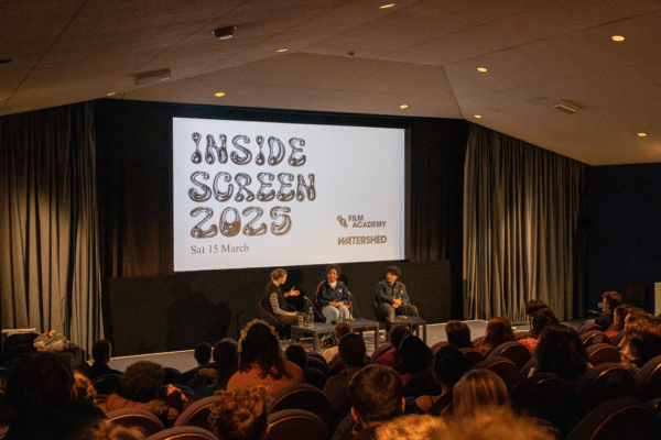 Shot of the audience in Watershed Cinema 1, with screen showing Inside Screen 2025 and Jess Wheeler, Shakira Newton and Alysha Christal in conversation on the stage