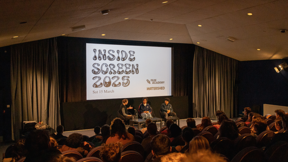 Shot of the audience in Watershed Cinema 1, with screen showing Inside Screen 2025 and Jess Wheeler, Shakira Newton and Alysha Christal in conversation on the stage