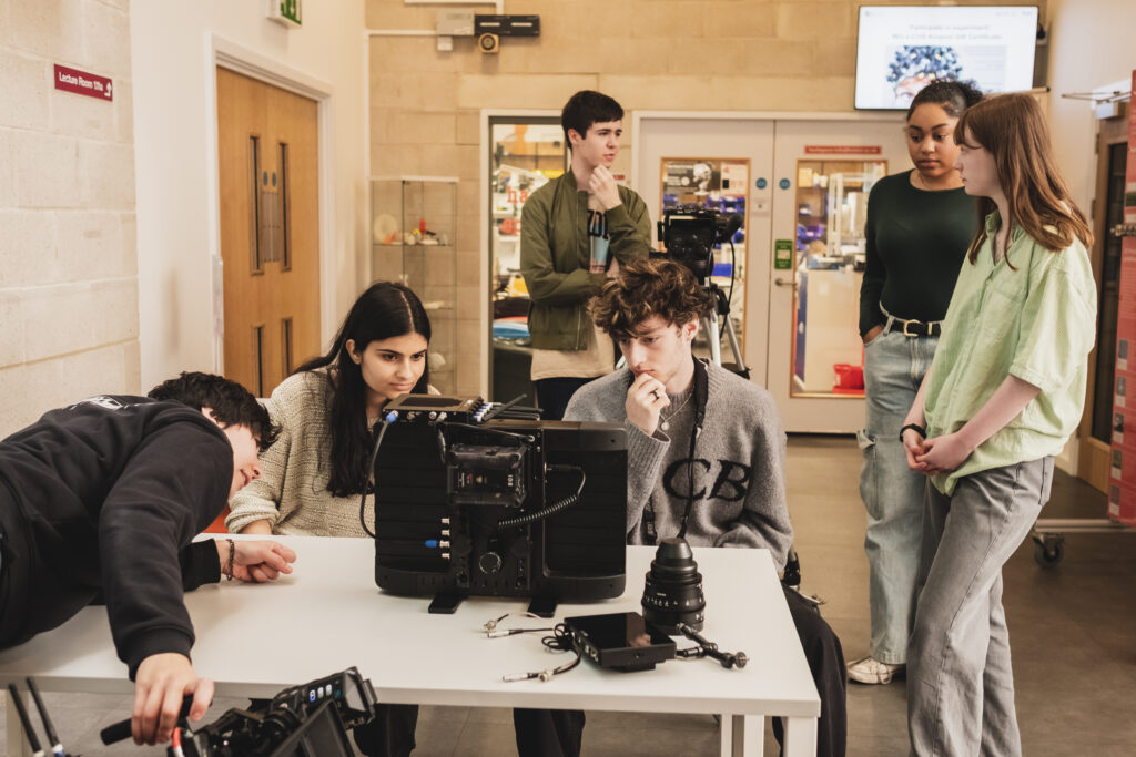 Young people gathered around a desk looking at a monitor surrounded by filmmaking equipment