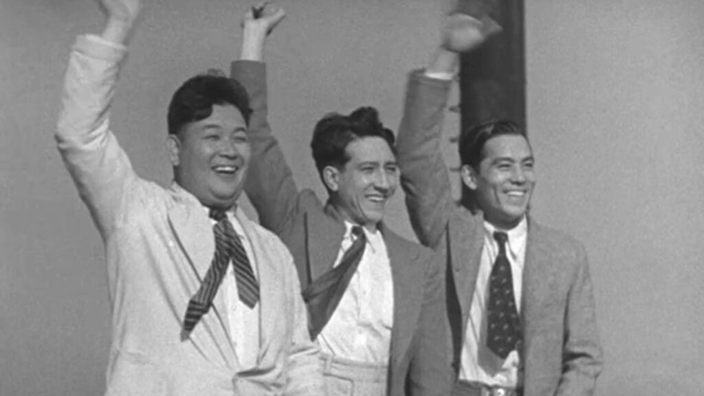 Three men wearing blazers and ties wave.