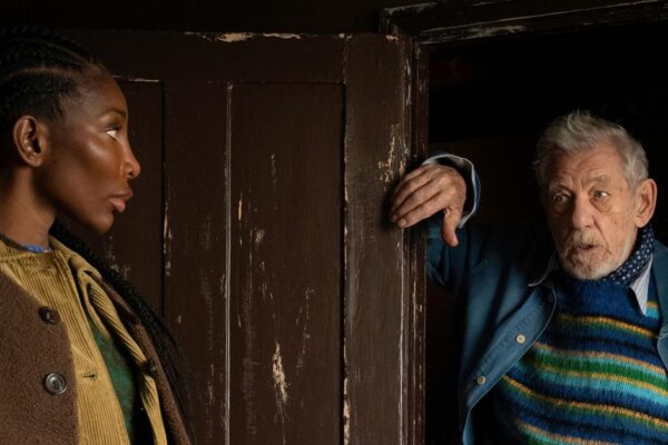 Still from The Christophers of Michaela Coel and Ian McKellen by a dark brown wooden door.