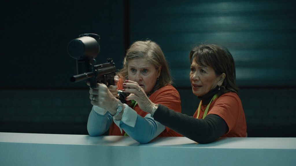 Still from A Shot At Art - two people wearing orange shirts, one holding a paintball gun.