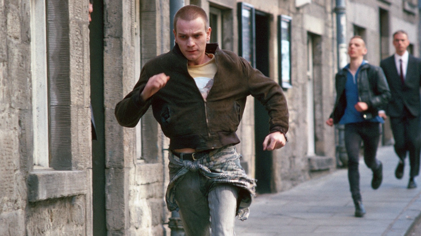 Trainspotting Still - a man running away from two men behind him.