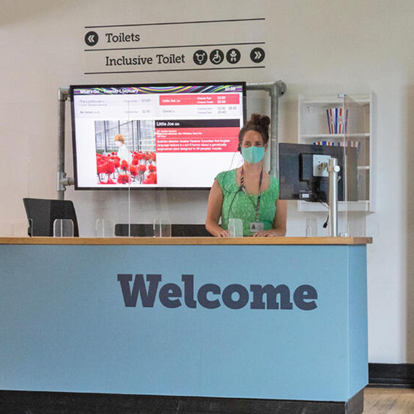 Photo a woman standing up at a reception desk, with the word welcome on it