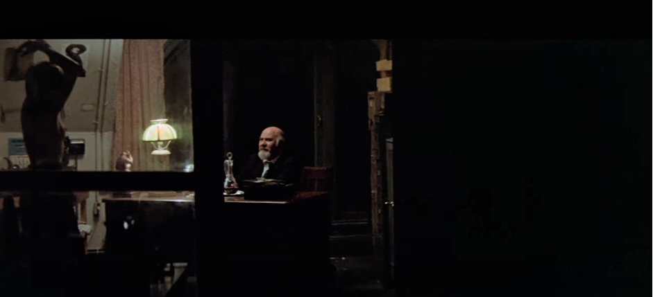 an image of a male sitting on a desk and a women standing near the desk in Klute 