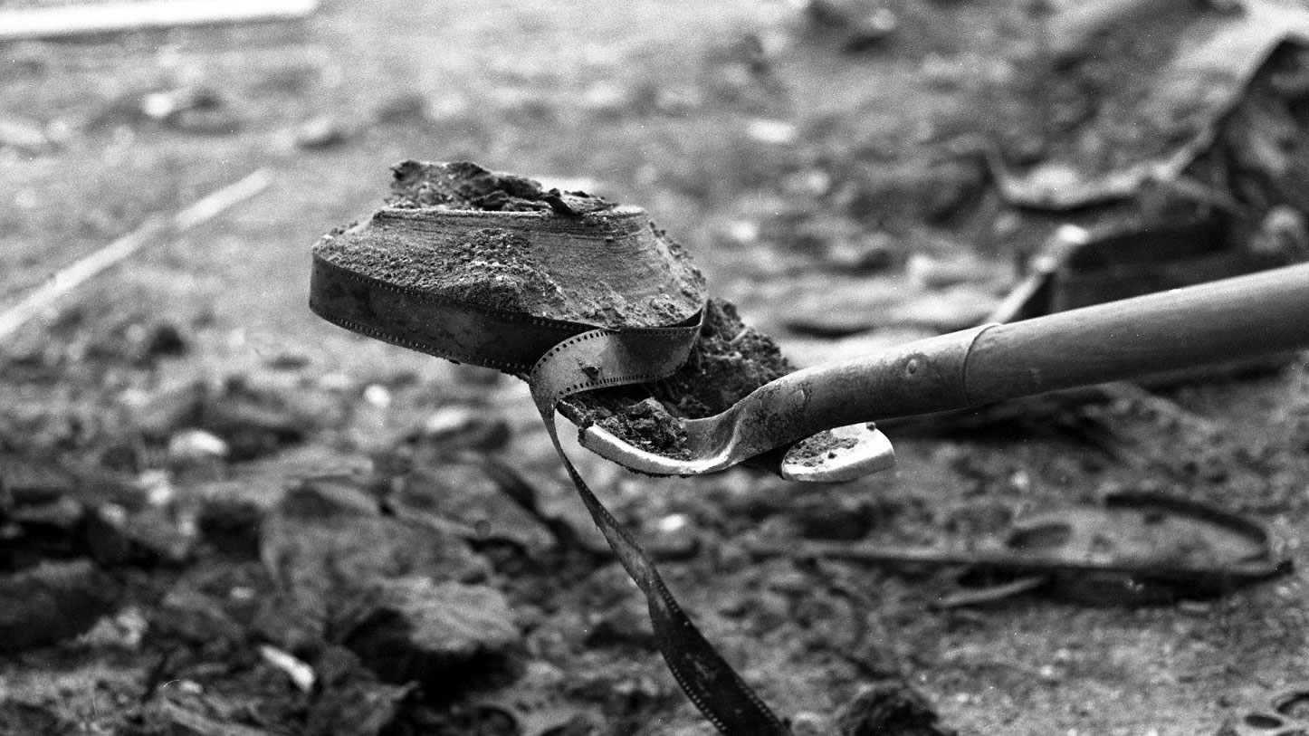 Photo of a shovel lifting a reel of film out of the ground