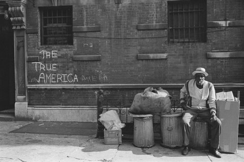Photograph by Ernest Cole of a man sitting on some dustbins.