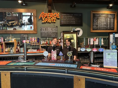 Photo of two people ready to serve behind the bar.