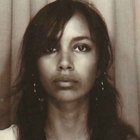 A young woman of colour looks into the camera with long dark hair and hoop earrings.
