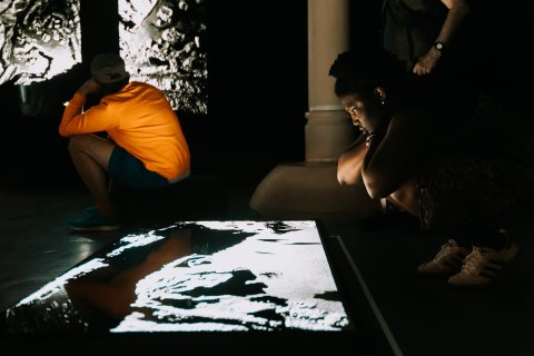 A young Black person is peering over an illuminated screen showing FRAMERATE: Pulse of the Earth.