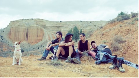 A group of four people seated on a rocky hillside, with a small dog beside them and a rugged landscape in the background.
