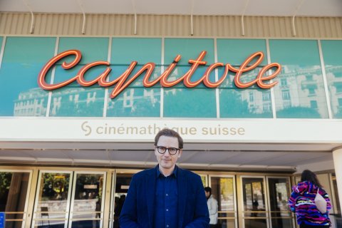 Man in blue jacket standing in front of Capitole cinéma building with turquoise glass and red neon sign.
