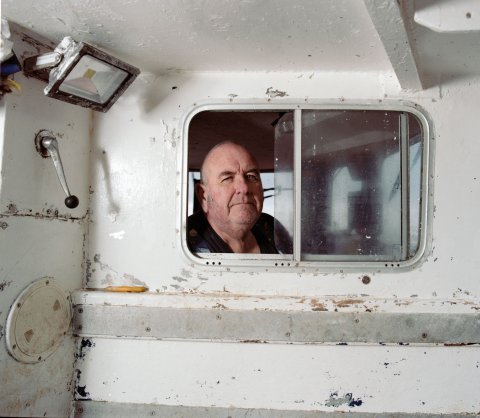 A man looks out towards the camera from a small window on a boat.