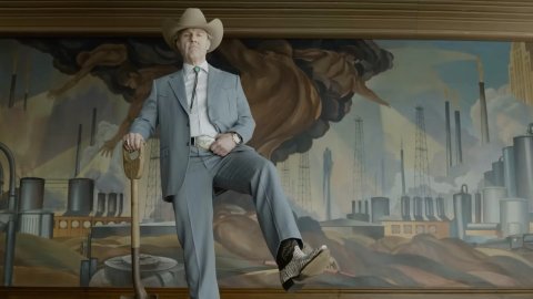 A man poses over-confidently with a shovel in front of a modernist painting.