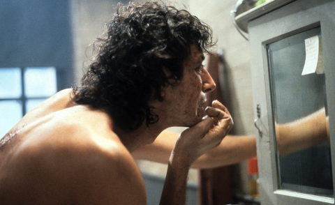 A man looks at his appearance in the mirror, looking concerned.