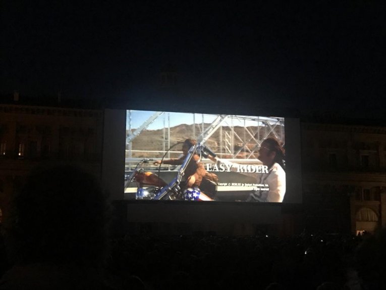 A photo of Easy Rider projected on to an outdoor cinema screen in a square in Italy