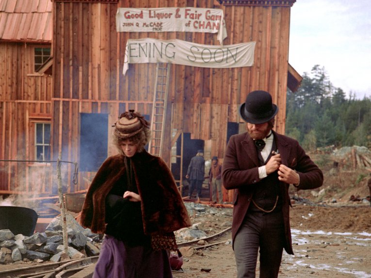 Photo of a man and woman in American turn of the century costume in front of a timber building