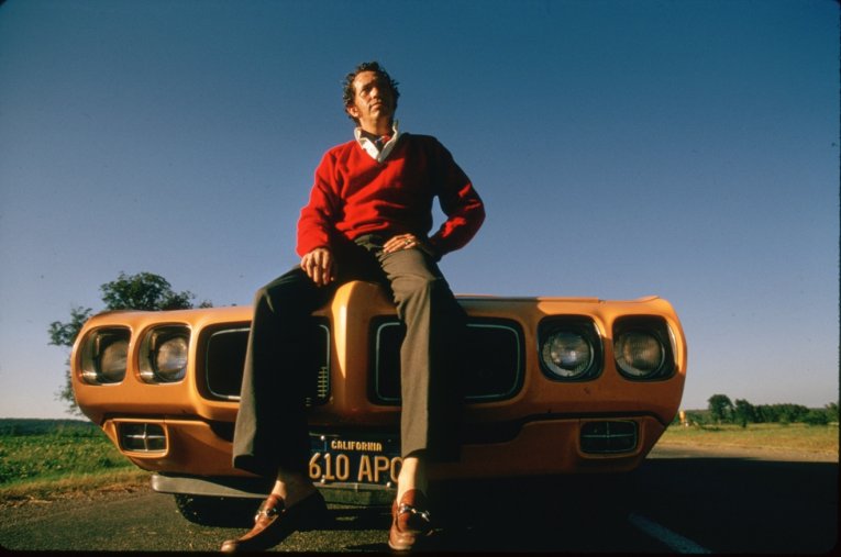 Photo of a man sat on the bonnet of a high powered American car