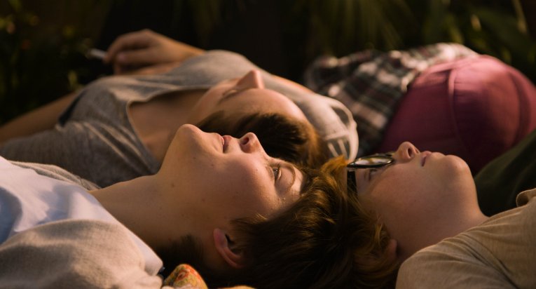 A still from Girls Lost. Three young people lie on their backs, looking to the sky. Their heads touch.
