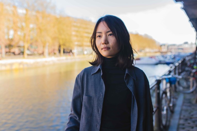 A woman in a black leather jacket. Behind her we see a harbour.