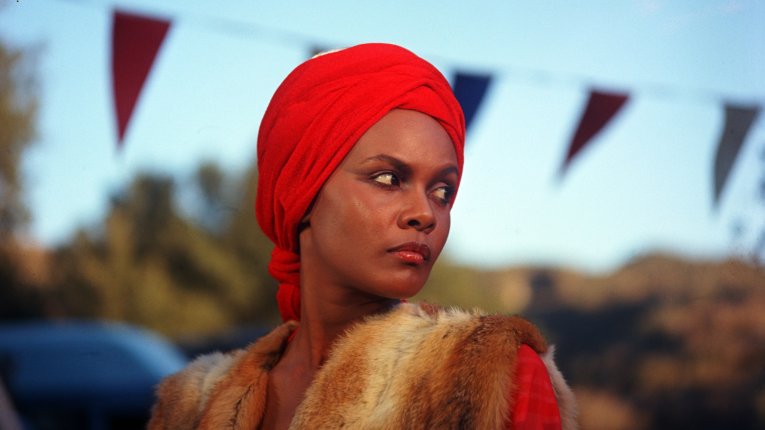 A woman wearing a read headscarf is looking off into the distance.