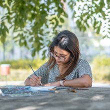 Woman seated outside painting at a table.