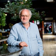 Photo of Dick Penny. He is a man with glasses, white hair and a blue shirt standing in Watershed's café