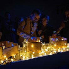 Lights and glass items are displayed on a counter, people are looking at them and interacting with them.