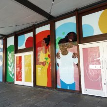 Exterior shot of Watershed with blue wood panelling displaying the Watershed logo and vinyls of smiling people covering the windows.