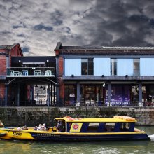 Exterior shot of Watershed Building and the harbour with a yellow ferry boat going past