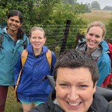 Four people smiling and taking a selfie in the wet and drizzly countryside.