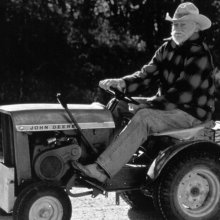 An older man sits on a John Deere tractor.