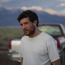 A man wearing a white t-shirt looks off into the distance.