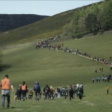 A photo of a large group of people walking up a grassy hill.