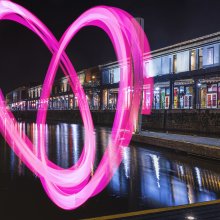 Watershed building at night, shot from the water, with a large pink heart drawn across the whole building.