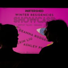 Silhouettes of two figures from the shoulders up. Before them is a neon pink sign, reading "Watershed Winter Residencies Showcase".