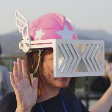 A person wearing a pink helmet with wings on, and a large rectangular viser over their eyes.