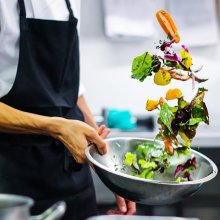 shot of chef's hand tossing a salad into a silver bowl